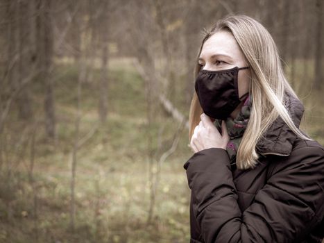 Beautiful european Women Wearing Protective Mask Outside Pretty young girl in medical black face mask in a forest. covid19 concept. modern reality. copy space. 2020, allergy. Autumn season. Copy space