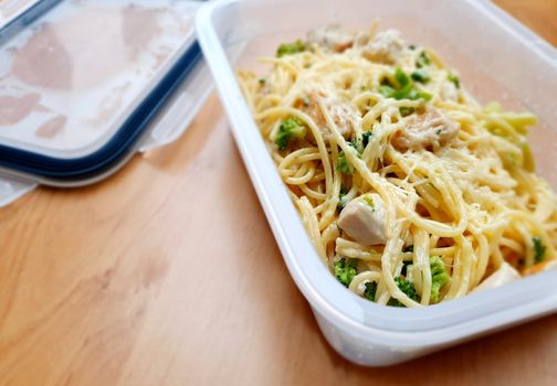 Takeaway food in plastic box. Spaghetti with broccoli, chicken meat and parmesan.