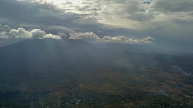 volcano with cloudy clear sky. Mount Merapi in Indonesia. Cloudy sky with a volcano in the background. Clouds around the top of the mountain. The sun's rays shine through the clouds.