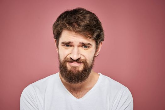 Emotional bearded man in white T-shirt discontent pink background. High quality photo
