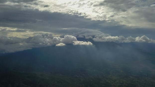 volcano with cloudy clear sky. Mount Merapi in Indonesia. Cloudy sky with a volcano in the background. Clouds around the top of the mountain. The sun's rays shine through the clouds.