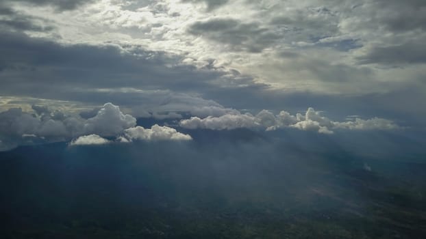 volcano with cloudy clear sky. Mount Merapi in Indonesia. Cloudy sky with a volcano in the background. Clouds around the top of the mountain. The sun's rays shine through the clouds.