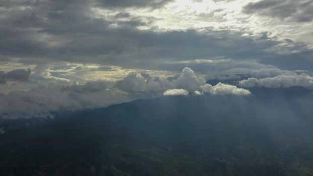 volcano with cloudy clear sky. Mount Merapi in Indonesia. Cloudy sky with a volcano in the background. Clouds around the top of the mountain. The sun's rays shine through the clouds.