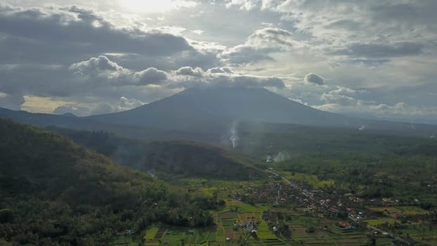 volcano with cloudy clear sky. Mount Merapi in Indonesia. Cloudy sky with a volcano in the background. Clouds around the top of the mountain. The sun's rays shine through the clouds.