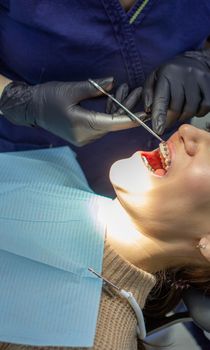 A woman with dental braces visits an orthodontist in the clinic, in a dental chair. during the procedure of installing the arch of braces on the upper and lower teeth. The dentist is wearing gloves and has dental instruments in his hands. The concept of dentistry