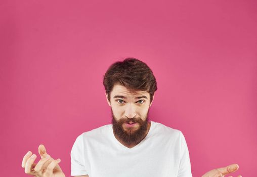 Happy young man on a pink background in a white T-shirt and a thick beard gesticulate with his hands. High quality photo