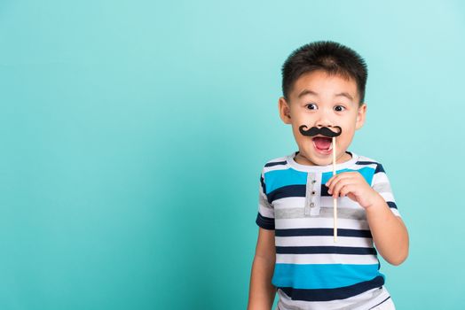 Funny happy hipster kid holding black mustache props for the photo booth close face, studio shot isolated on a blue background, Men health awareness, Prostate Cancer Awareness