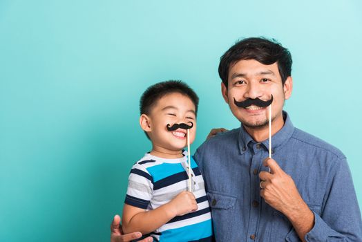 Family funny happy hipster father and his son kid holding black mustache props for the photo booth close face, studio shot isolated on a blue background, November men health awareness