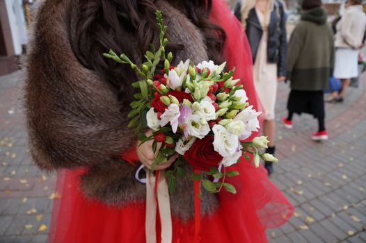 bride in a red dress holds a wedding bouquet, close-up
