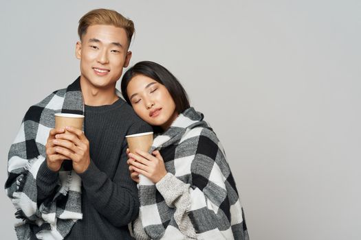 Young couple taking shelter with a plaid blanket warming drink coolness family