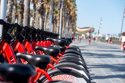 Barcelona, Spain - June 26, 2020: Bright red bicycles available for rent parked in a row at La Barceloneta. Concept of environmentally sustainable transport. Bike rental service Bicing.