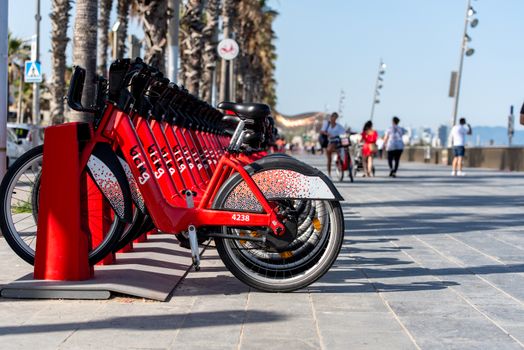 Barcelona, Spain - June 26, 2020: Bright red bicycles available for rent parked in a row at La Barceloneta. Concept of environmentally sustainable transport. Bike rental service Bicing.