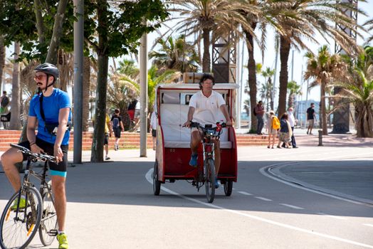 BARCELONA - JUNE 26, 2020: tuk tuk in Barceloneta beach with people in summer after COVID 19 on June 26, 2020 in Barcelona, ​​Spain.