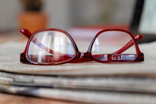 A pair of glasses on newspapers at a narrow foreground with a completely out of focus background.