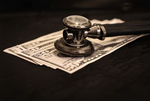 A stethoscope on three fifty dollar bills. Sepia toned photo