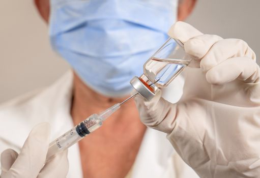 Needle of a syringe inside a vaccine container. Handling hands are protected by gloves