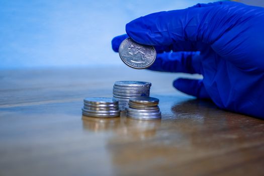 Protected hand with a blue glove holding a quarter of dollar over a group of coins