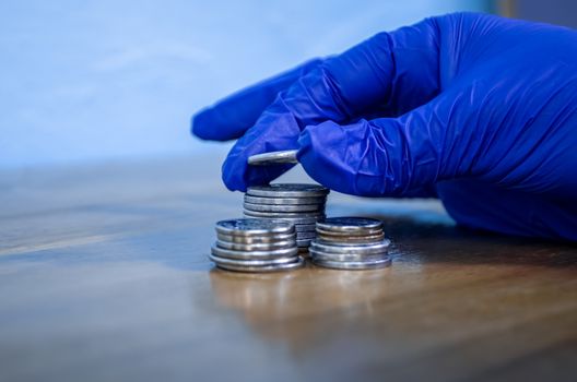 Protected hand with a blue glove manipulating money coins