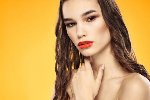 Beautiful brunette naked shoulders bright makeup red lips hairstyle close-up yellow background. High quality photo