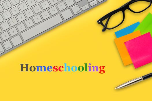 HOMESCHOOLING text with computer keyboard, eyeglasses, sticky notes and fountain pen on yellow background. Business and education concept