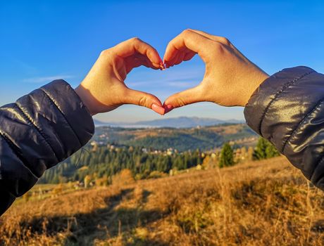 Romance and love. The girl folded her hands in the form of a heart against the background of mountains covered with trees, which are illuminated by the rising sun. A meeting of dawn in the mountains.