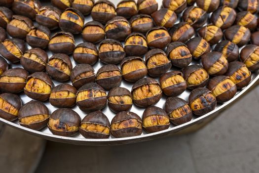 Roasted chestnuts nicely laid out on an iron tray. Close up, top view.