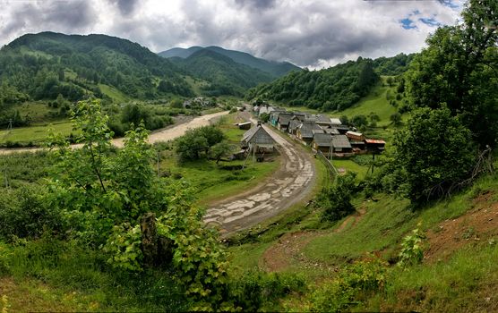 Ecotourism. Rural landscape. An old village in a picturesque place among the hills and mountains overgrown with green trees. The road passes through the village.
