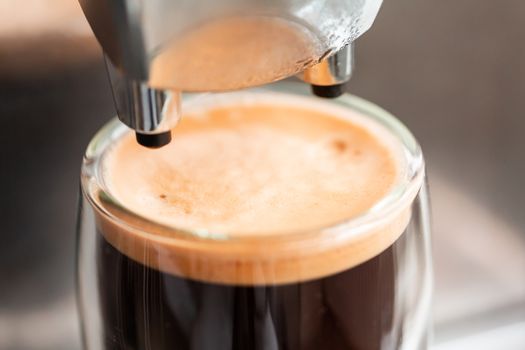 Coffee espresso streaming from coffee machine and pouring into glass. Home making hot Espresso. Flowing fresh ground coffee. Drinking roasted black coffee in the morning.