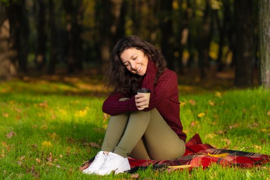 Pretty girl enjoys autumn and the beauty of nature sitting on a green lawn in the park. Autumn mood.