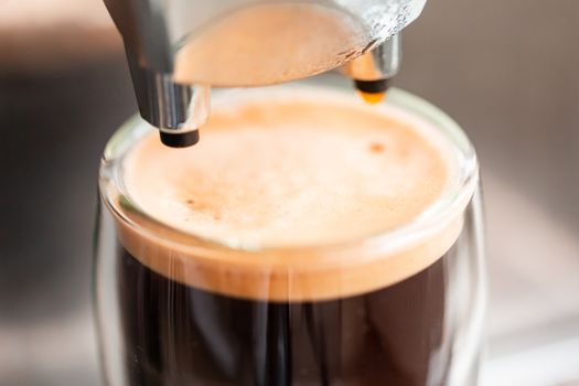 Coffee espresso streaming from coffee machine and pouring into glass. Home making hot Espresso. Flowing fresh ground coffee. Drinking roasted black coffee in the morning.