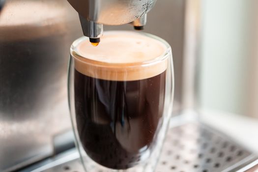 Coffee espresso streaming from coffee machine and pouring into glass. Home making hot Espresso. Flowing fresh ground coffee. Drinking roasted black coffee in the morning.