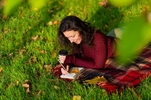 Person writes notes lying on the lawn in the autumn park. Solitude with yourself.