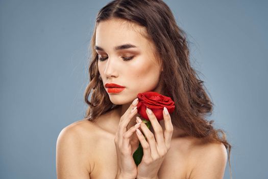 Woman portrait with red rose near the face on gray background and makeup curly hair. High quality photo