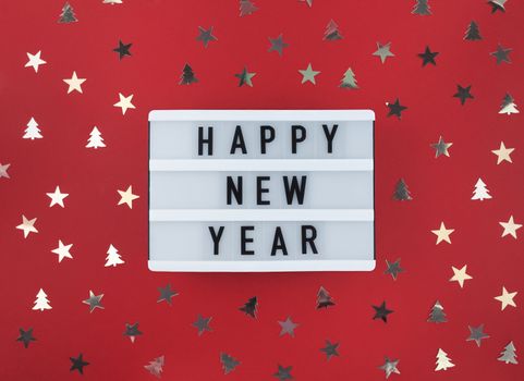 Happy New Year greeting on light box and confetti on red background.