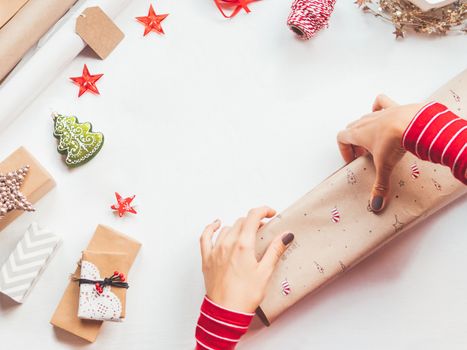 Top view on table with Christmas decorations. Woman draws New Year symbols on craft paper and wraps presents. Flat lay with copy space.