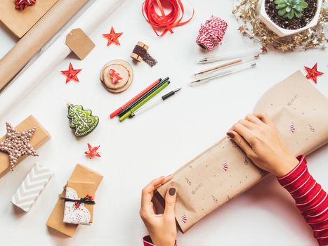 Top view on table with Christmas decorations. Woman draws New Year symbols on craft paper and wraps presents. Flat lay.