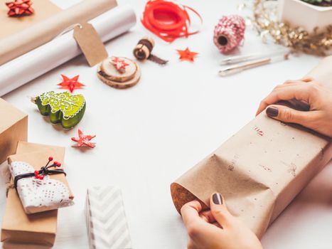 Table with Christmas decorations. Woman draws New Year symbols on craft paper and wraps presents. Flat lay with copy space.