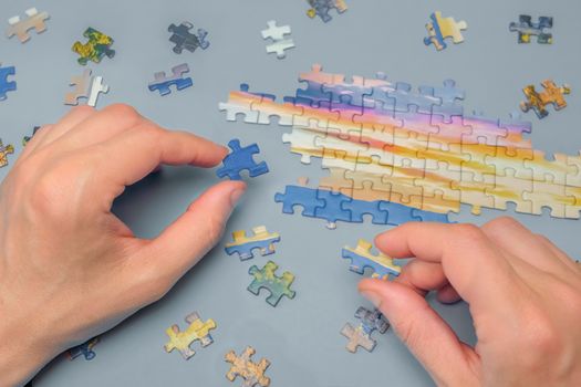 Assembling Jigsaw Puzzle. Male Hands Connect the Pieces of a Jigsaw Puzzle. Indoor Leisure Activity. Playing Calm Board Game. Pastime, a Hobby. Unfinished Jigsaw Puzzle. Finding a Solution. Top View