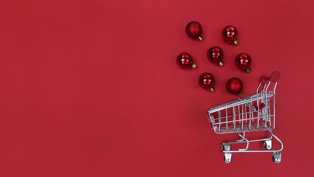 Supermarket trolley and Christmas tree baubles on red paper.