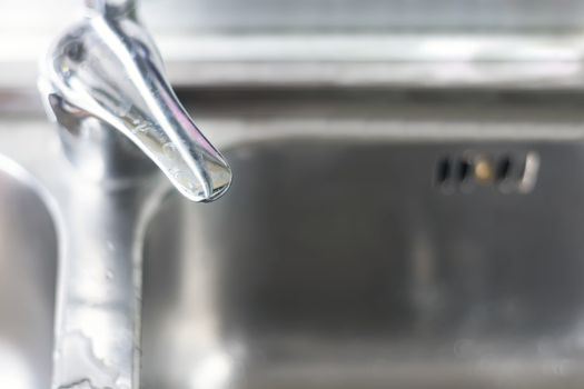 Top view of the mixer lever of a chrome waterfall tap of a domestic kitchen with the aluminum sink in the background. Limestone on the lever