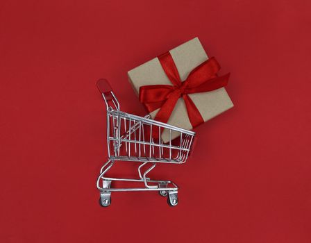 Supermarket trolley and gift box on red background. Shopping concept.