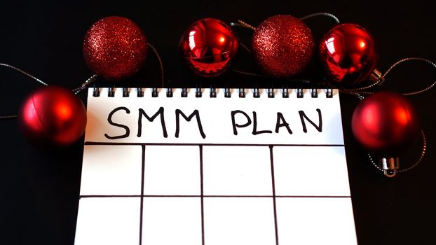 Freelance project. SMM plan blank. White sheet on a black festive background with red Christmas balls