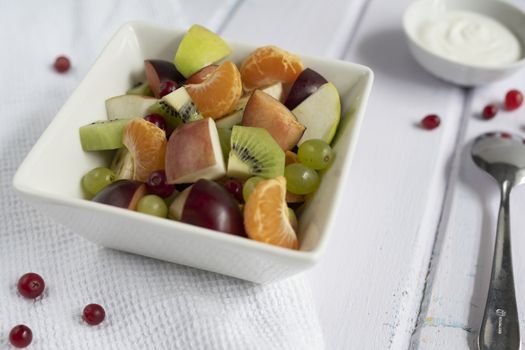 fresh fruit salad in glass bowl on white wooden background.