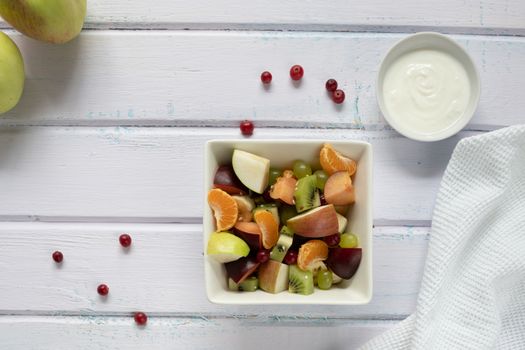 fresh fruit salad in glass bowl on white wooden background.
