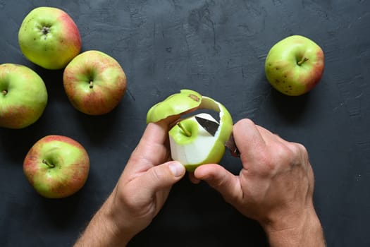 Piece of cut and peeled apple, peels and seeds, on black background.