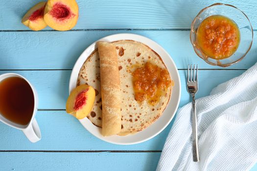 large pancakes with jam, tea and peaches on blue background.