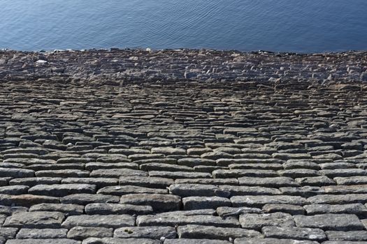 Looking down a sloping reservoir stone wall, a full frame abstract texture image is formed. Deep blue water ripples form good copy space.
