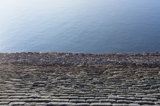 Half and half full frame background texture. Bright blue sunny reservoir water against warm grey linear rock wall. Plain with loads of copy space