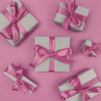 Gift boxes wrapped in a craft paper with soft pink ribbons and bows. Festive monochrome flat lay.