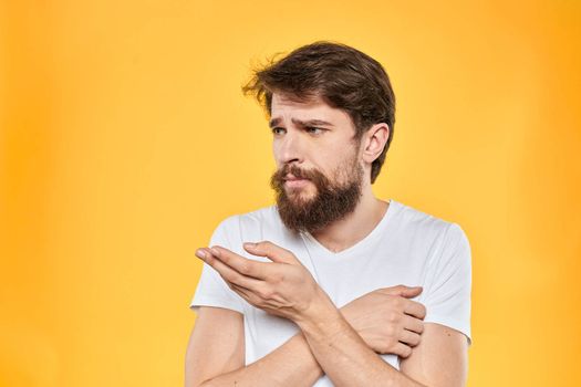 Man in white t-shirt emotions studio gestures with hands displeased facial expression yellow background. High quality photo